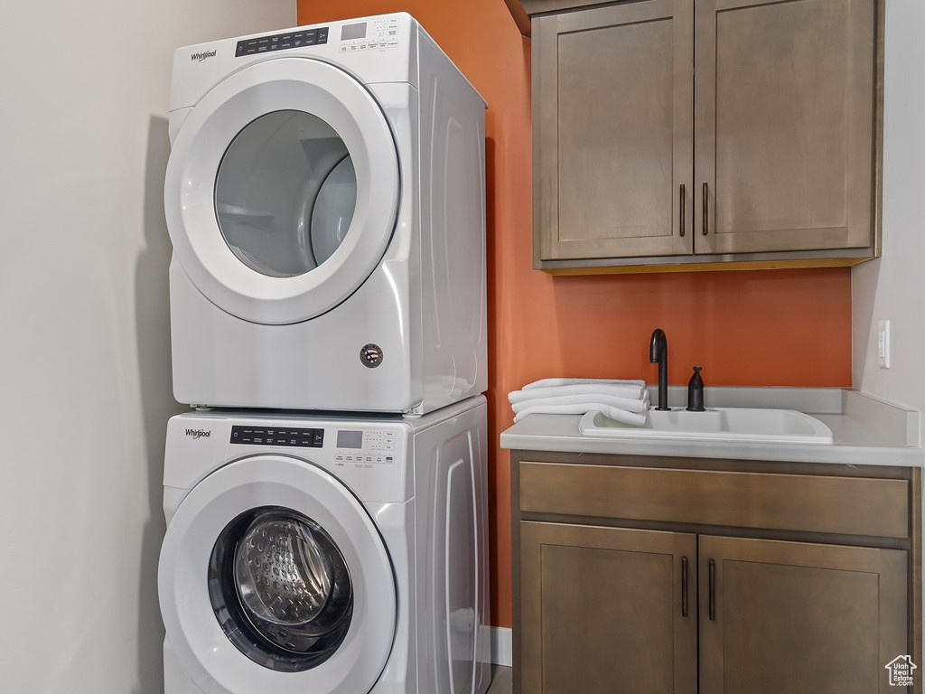 Washroom with stacked washing maching and dryer, sink, and cabinets