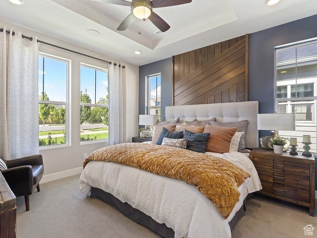 Carpeted bedroom featuring ceiling fan and a raised ceiling