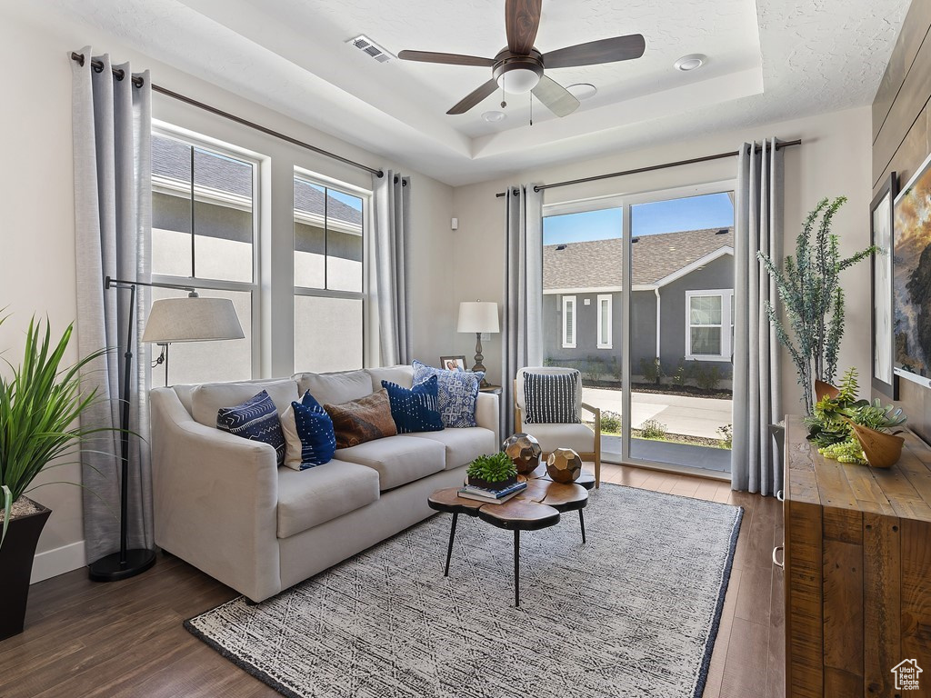 Living room with plenty of natural light, dark hardwood / wood-style floors, ceiling fan, and a raised ceiling