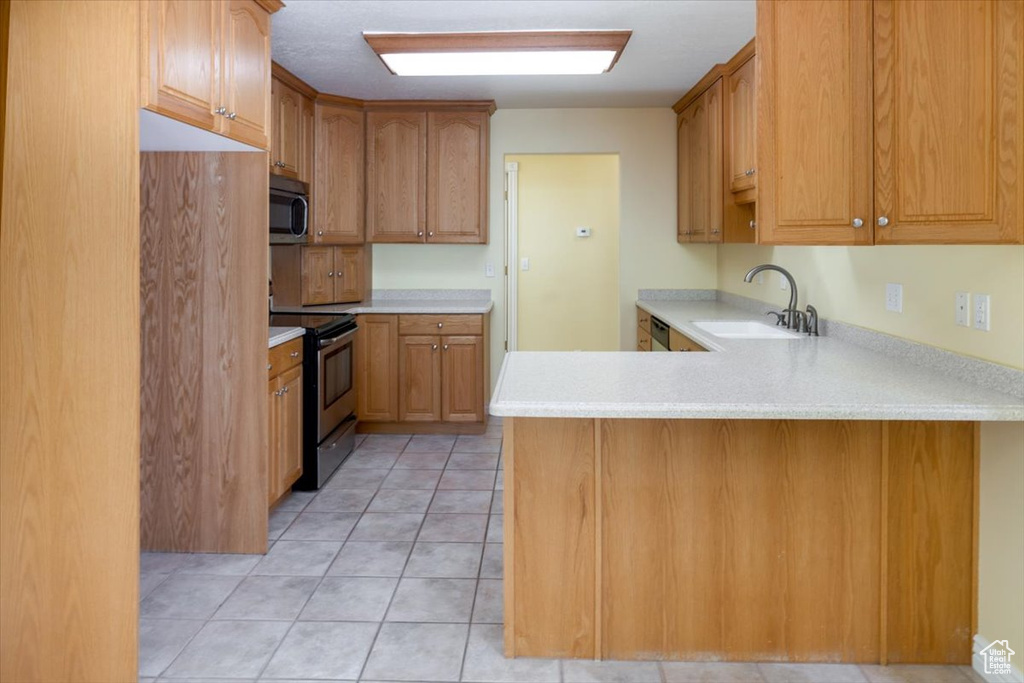 Kitchen with sink, kitchen peninsula, stainless steel appliances, and light tile patterned floors