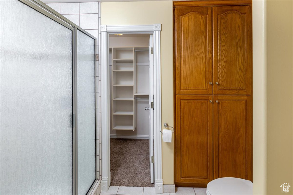 Bathroom with toilet, a shower with door, and tile patterned flooring