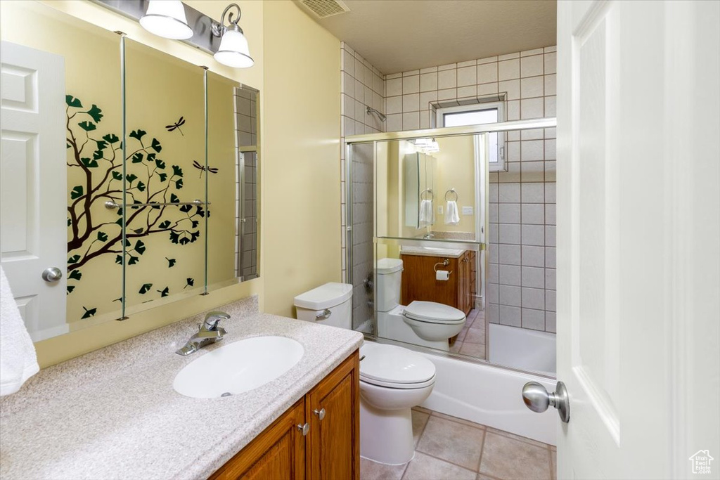 Full bathroom with vanity, tile patterned flooring, bath / shower combo with glass door, and toilet