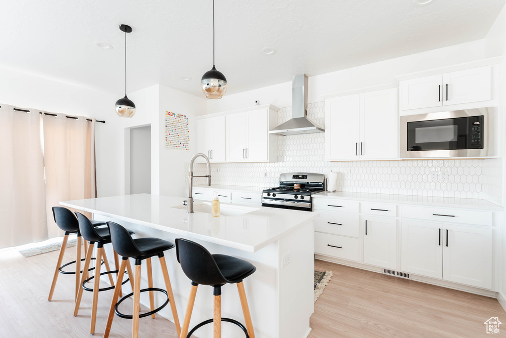 Kitchen featuring black microwave, tasteful backsplash, wall chimney range hood, light wood-type flooring, and stainless steel gas range oven
