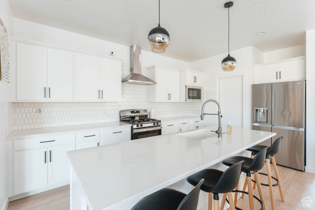 Kitchen with light hardwood / wood-style flooring, backsplash, appliances with stainless steel finishes, wall chimney exhaust hood, and a center island with sink