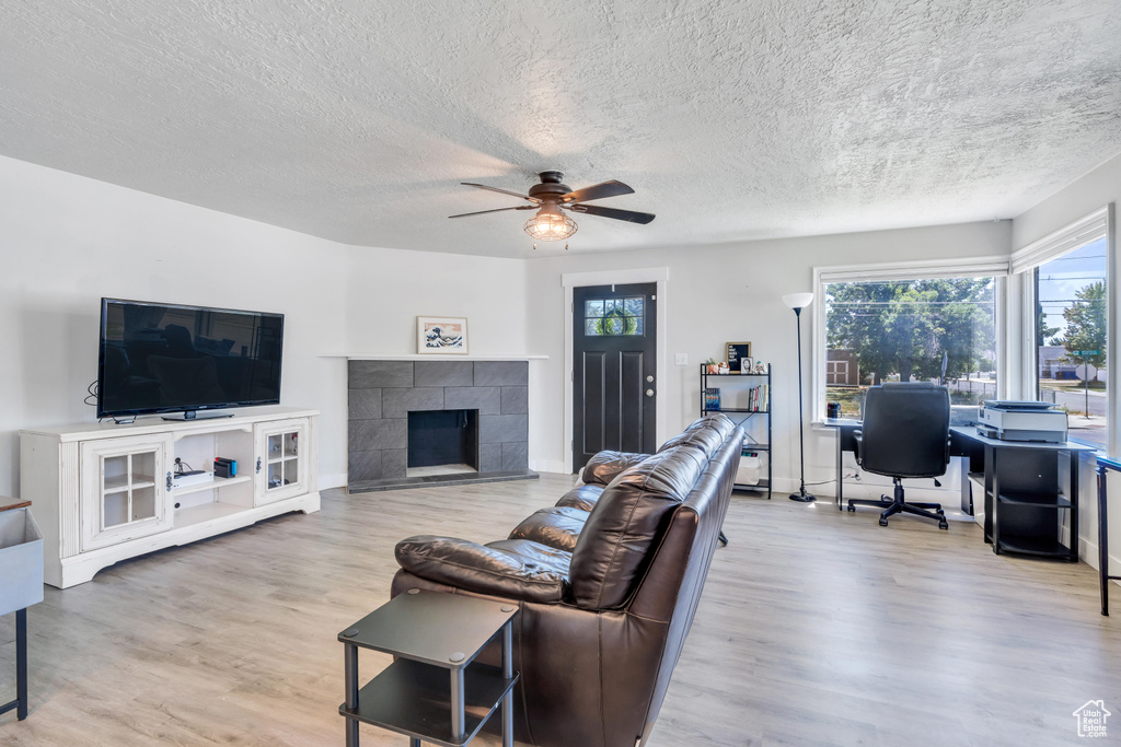 Living room featuring a fireplace, light hardwood / wood-style floors, a textured ceiling, and ceiling fan