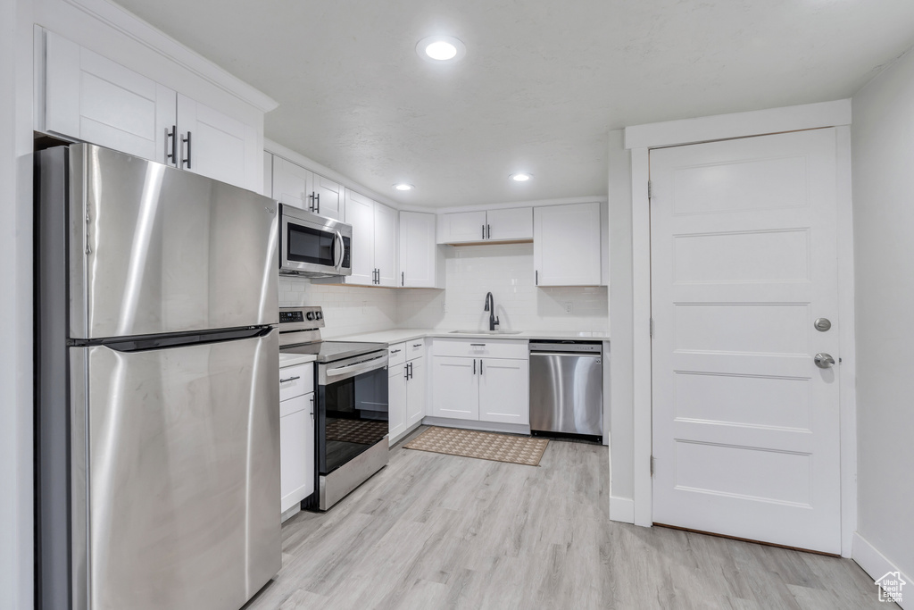 Kitchen featuring stainless steel appliances, white cabinets, sink, light hardwood / wood-style floors, and backsplash