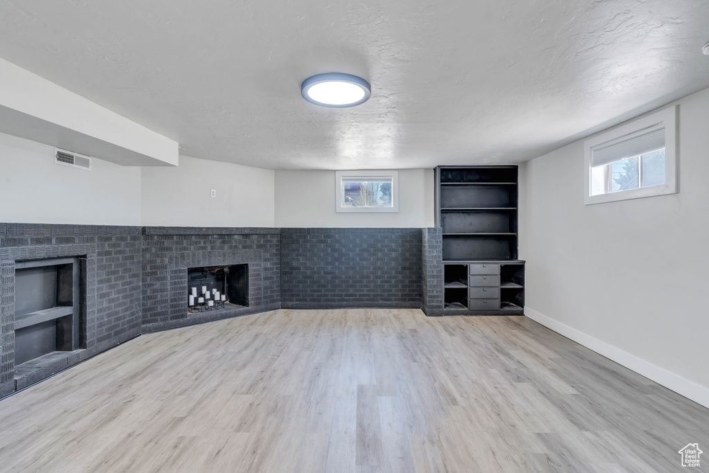 Unfurnished living room featuring built in features, light wood-type flooring, a fireplace, and plenty of natural light