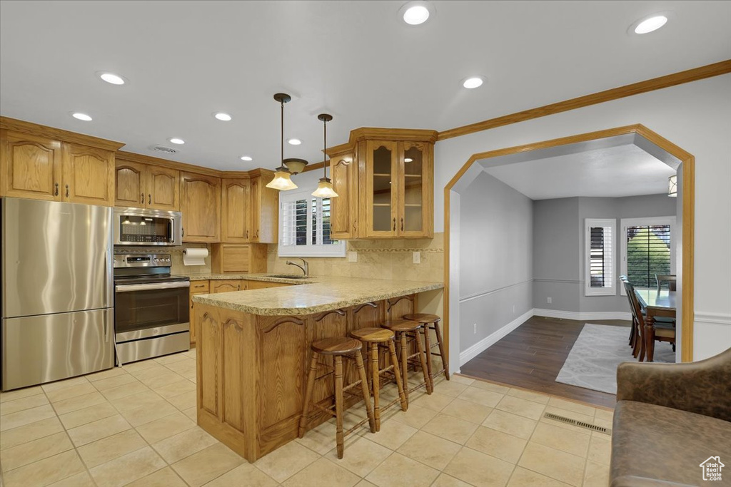 Kitchen with kitchen peninsula, backsplash, light hardwood / wood-style floors, light stone countertops, and appliances with stainless steel finishes