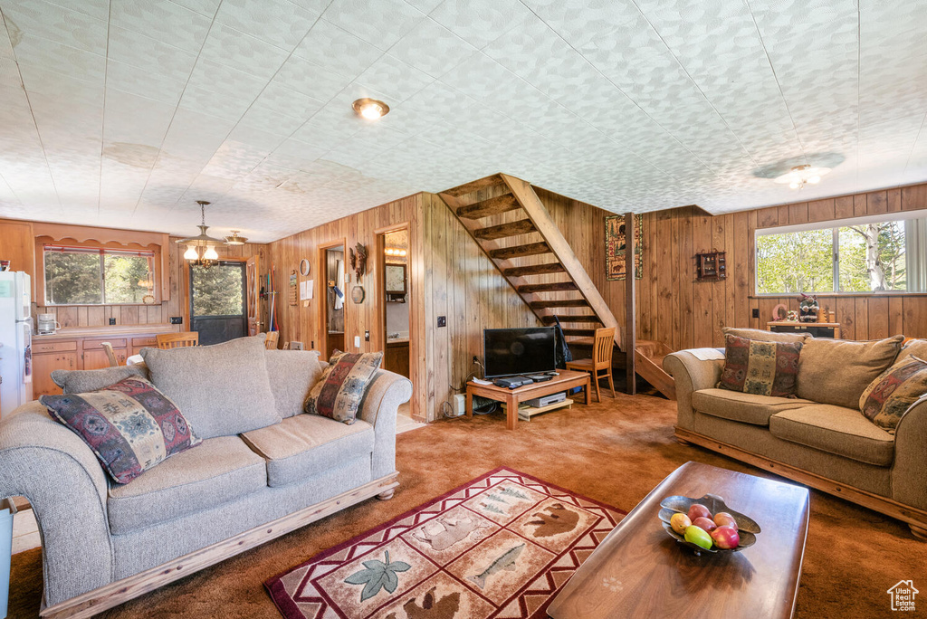 Carpeted living room with an inviting chandelier and wooden walls