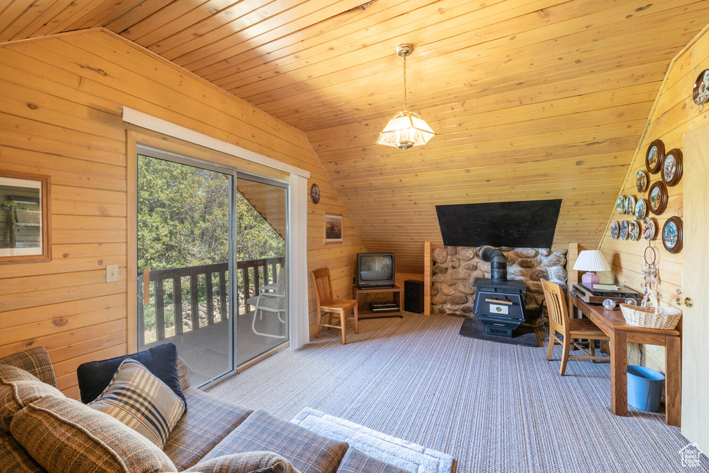 Living room featuring lofted ceiling, a wood stove, wood walls, wood ceiling, and carpet floors