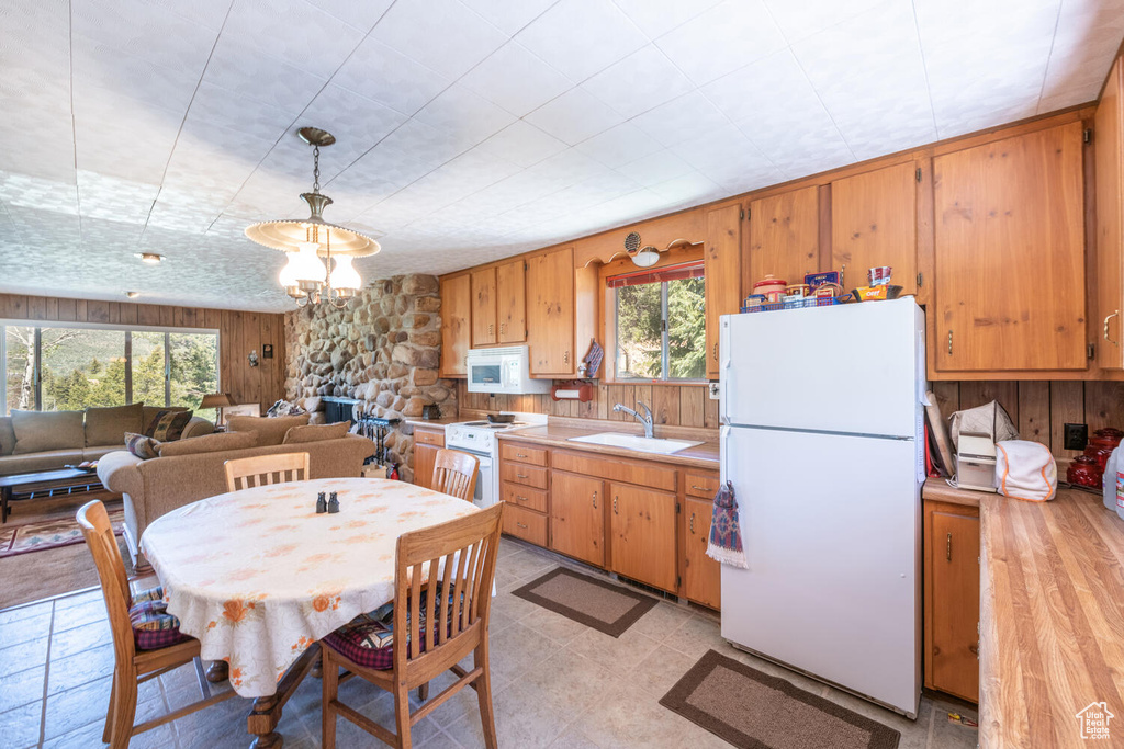 Kitchen featuring white appliances, light wood-type flooring, wood walls, pendant lighting, and sink