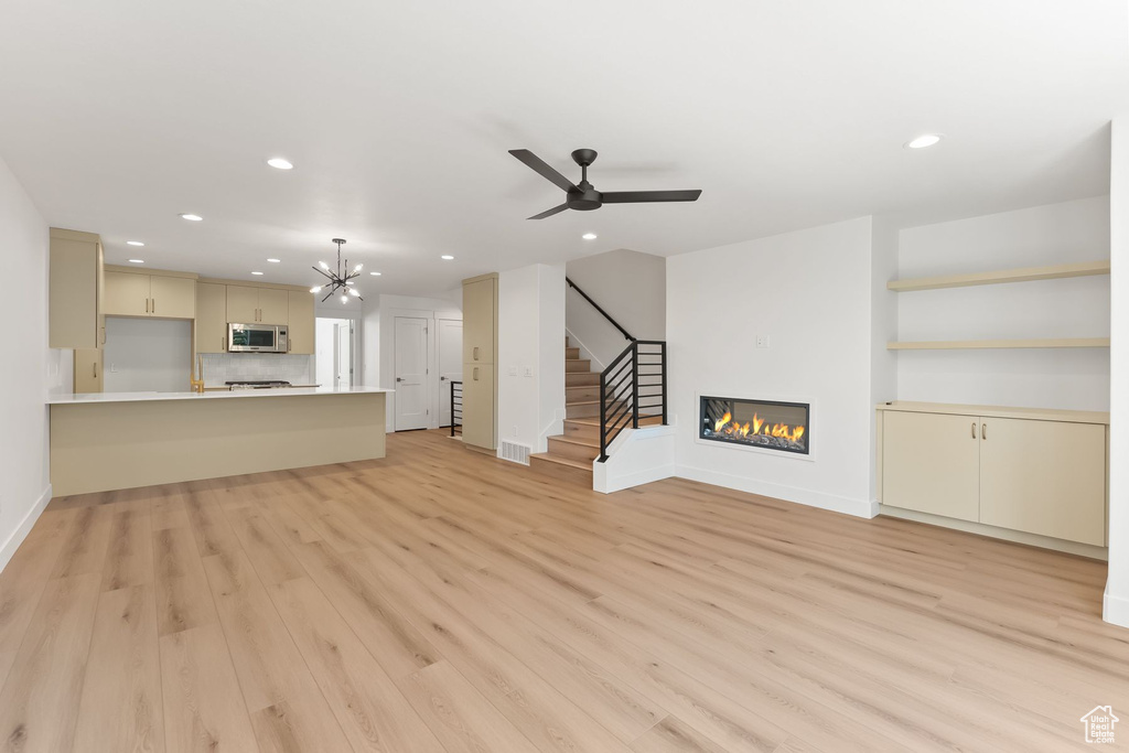 Unfurnished living room with ceiling fan with notable chandelier and light wood-type flooring