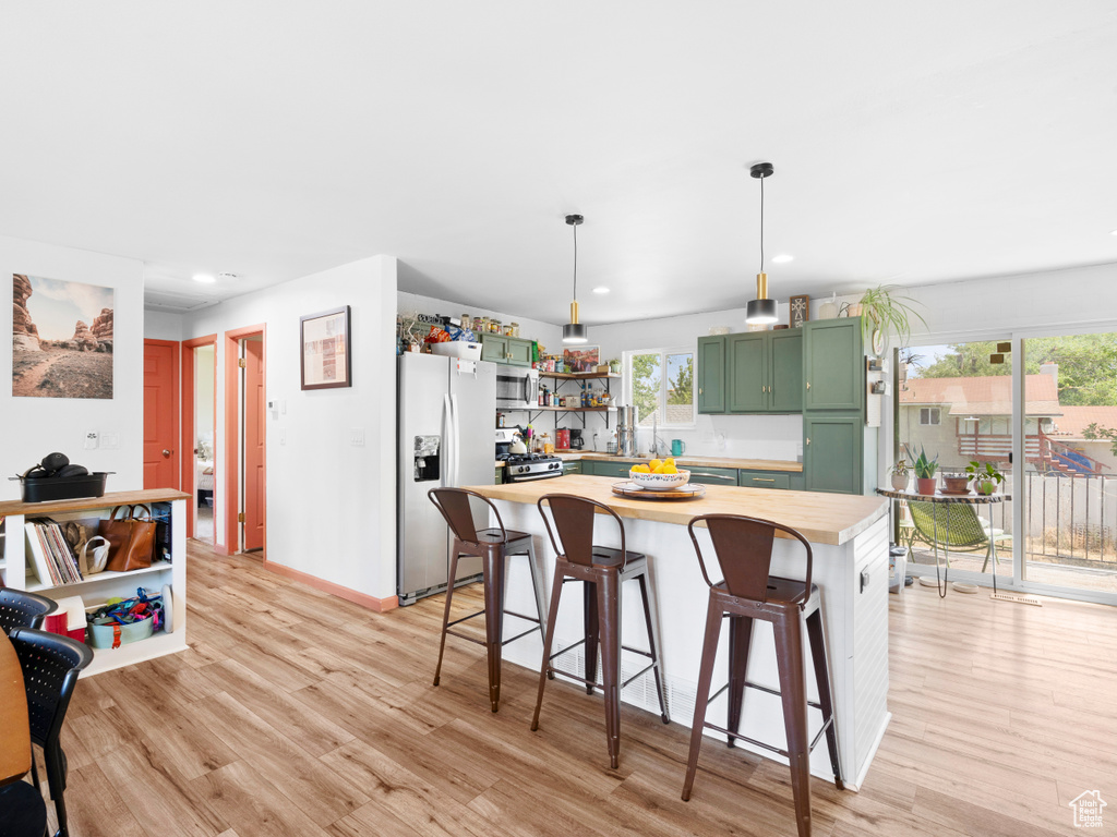 Kitchen featuring decorative light fixtures, butcher block counters, light wood-type flooring, appliances with stainless steel finishes, and green cabinetry