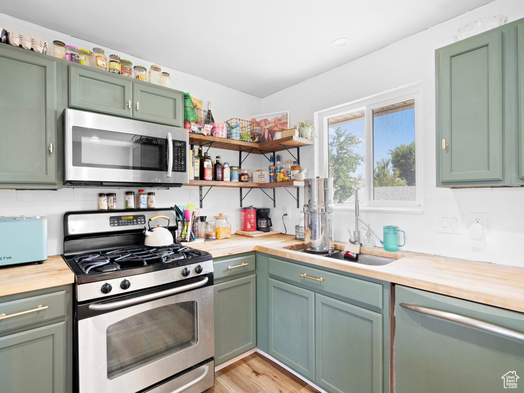 Kitchen with sink, green cabinets, appliances with stainless steel finishes, and light hardwood / wood-style floors