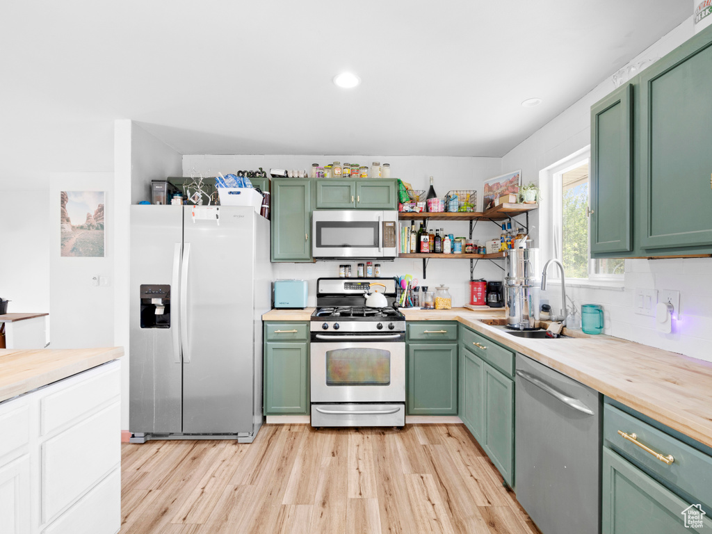 Kitchen with sink, green cabinetry, light wood-type flooring, and stainless steel appliances