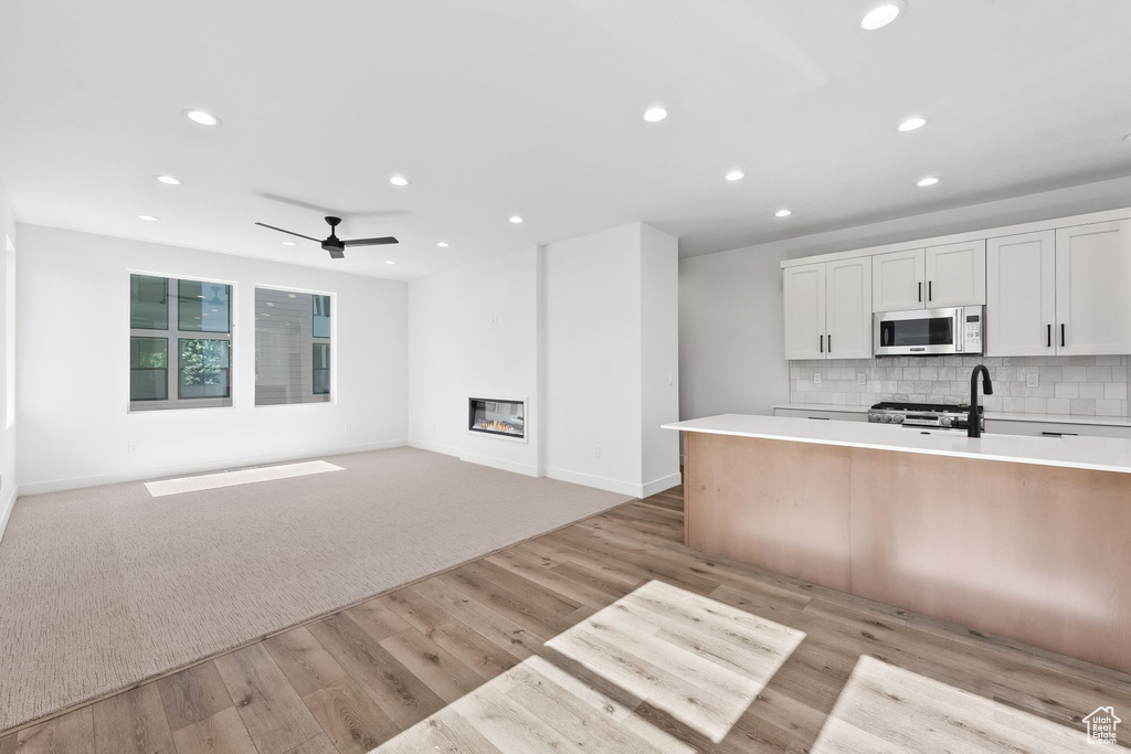 Kitchen with white cabinetry, backsplash, ceiling fan, light hardwood / wood-style floors, and a center island with sink