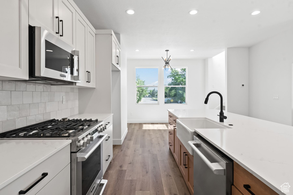 Kitchen with white cabinets, stainless steel appliances, light stone countertops, decorative backsplash, and hardwood / wood-style flooring