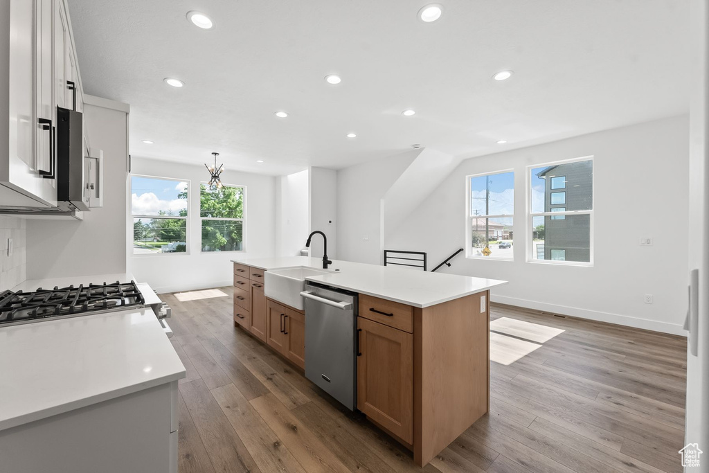 Kitchen with light hardwood / wood-style floors, dishwasher, and a kitchen island with sink