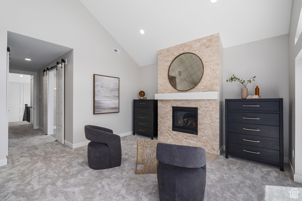 Interior space featuring a fireplace, light colored carpet, a barn door, and high vaulted ceiling