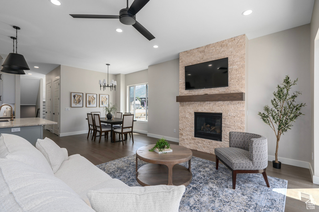 Living room featuring sink, dark hardwood / wood-style flooring, a fireplace, and ceiling fan with notable chandelier