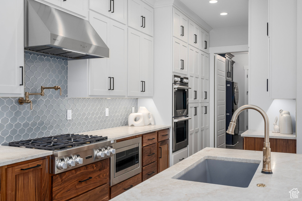 Kitchen featuring white cabinetry, wall chimney range hood, stainless steel appliances, sink, and backsplash