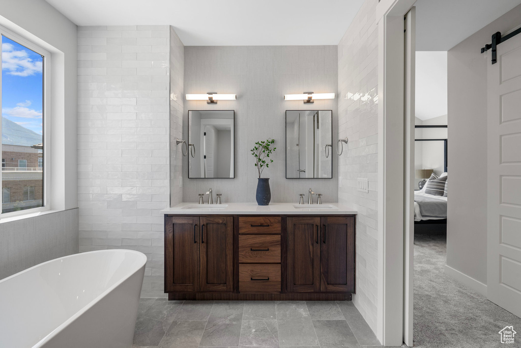 Bathroom with double vanity, tile walls, tile patterned floors, and a tub to relax in