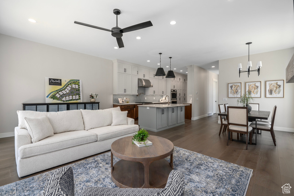 Living room with dark hardwood / wood-style floors, ceiling fan with notable chandelier, and sink