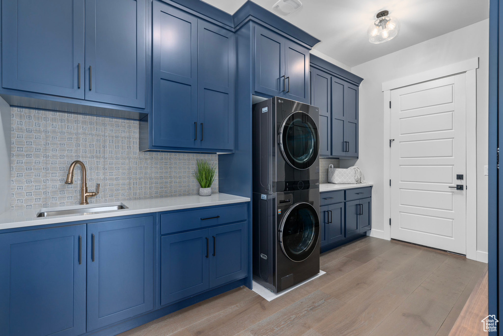 Washroom featuring cabinets, hardwood / wood-style floors, sink, and stacked washing maching and dryer