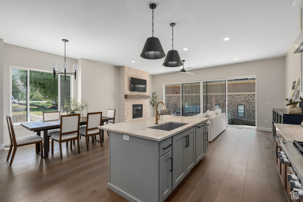 Kitchen with gray cabinetry, a stone fireplace, sink, a kitchen island with sink, and dark hardwood / wood-style floors