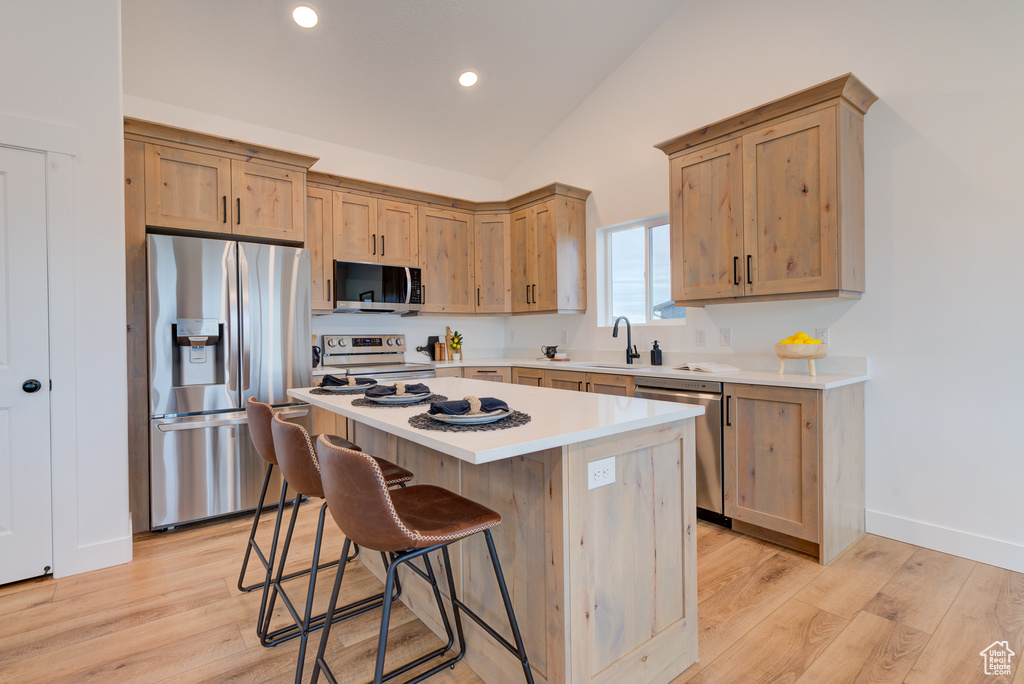 Kitchen with appliances with stainless steel finishes, a breakfast bar area, light hardwood / wood-style flooring, lofted ceiling, and a center island