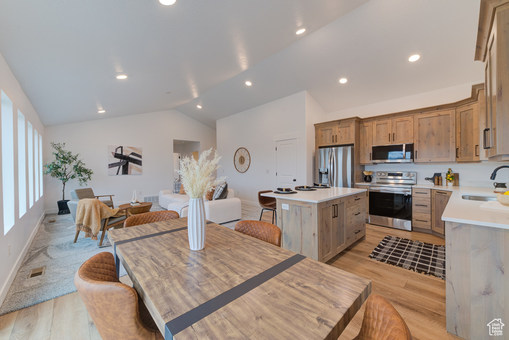 Kitchen featuring lofted ceiling, light hardwood / wood-style flooring, a center island, appliances with stainless steel finishes, and sink