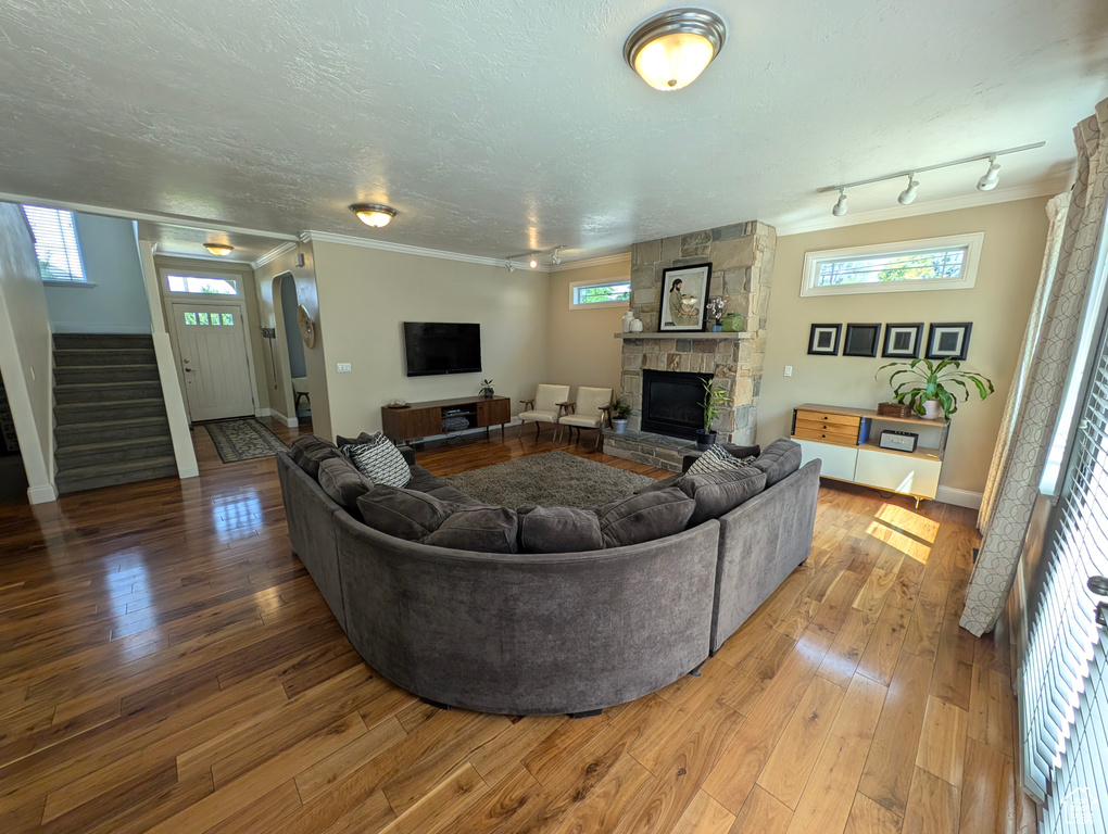 Living room featuring hardwood / wood-style flooring, a stone fireplace, track lighting, and a textured ceiling