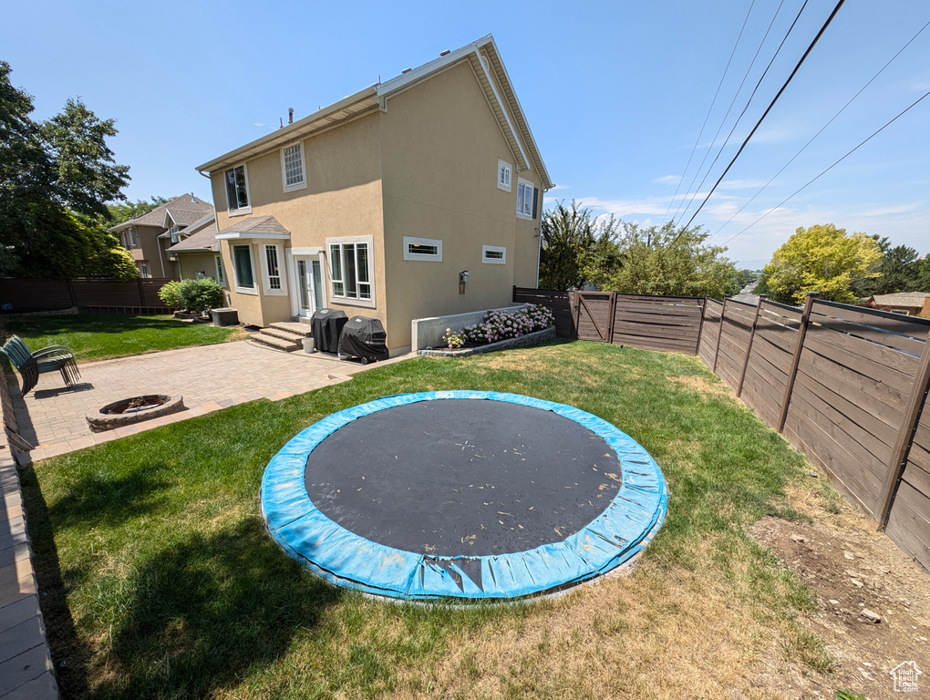 Exterior space featuring a trampoline, a patio, a lawn, and a fire pit