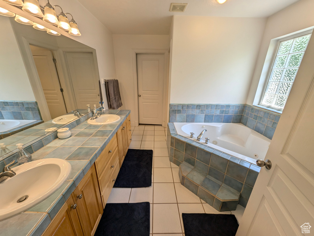 Bathroom with tile patterned flooring, tiled tub, and dual bowl vanity