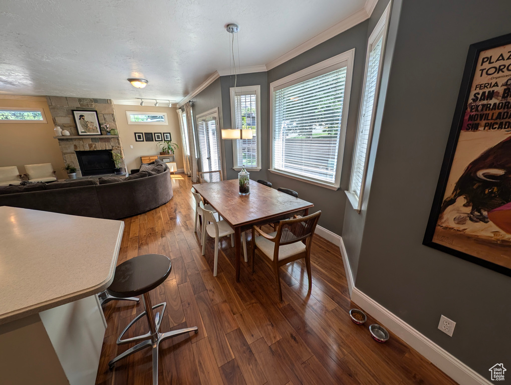 Dining space featuring a stone fireplace, crown molding, and dark wood-type flooring