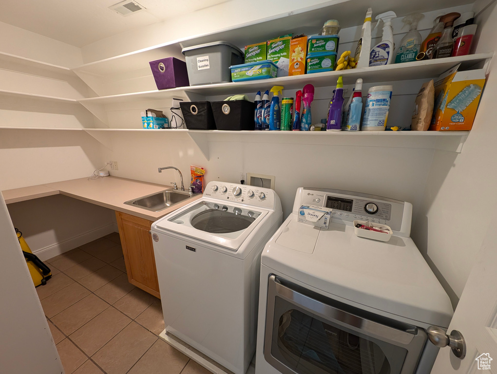 Clothes washing area with cabinets, washing machine and clothes dryer, sink, and light tile patterned floors