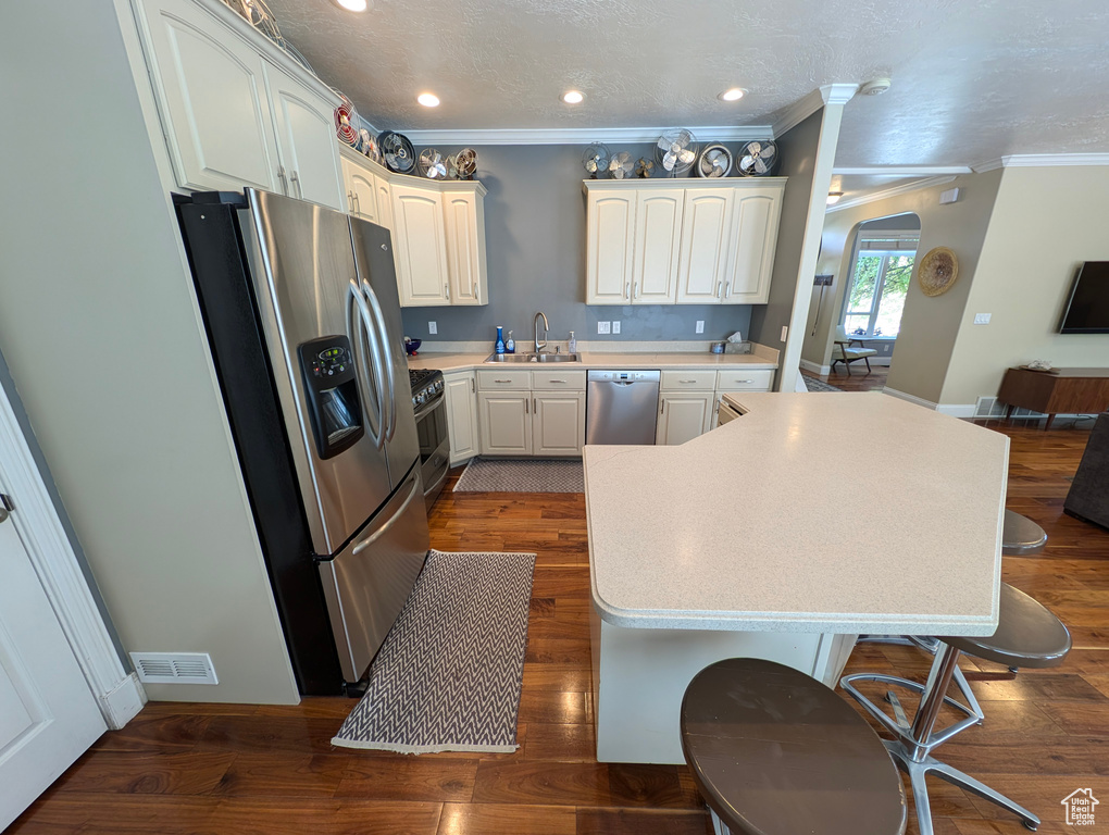 Kitchen featuring white cabinetry, crown molding, stainless steel appliances, hardwood / wood-style floors, and sink