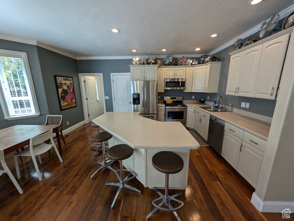 Kitchen featuring stainless steel appliances, a kitchen island, a kitchen breakfast bar, dark wood-type flooring, and ornamental molding