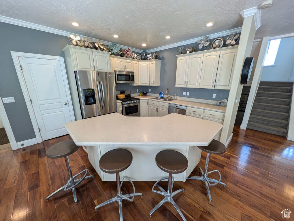 Kitchen with dark hardwood / wood-style floors, appliances with stainless steel finishes, sink, and ornamental molding