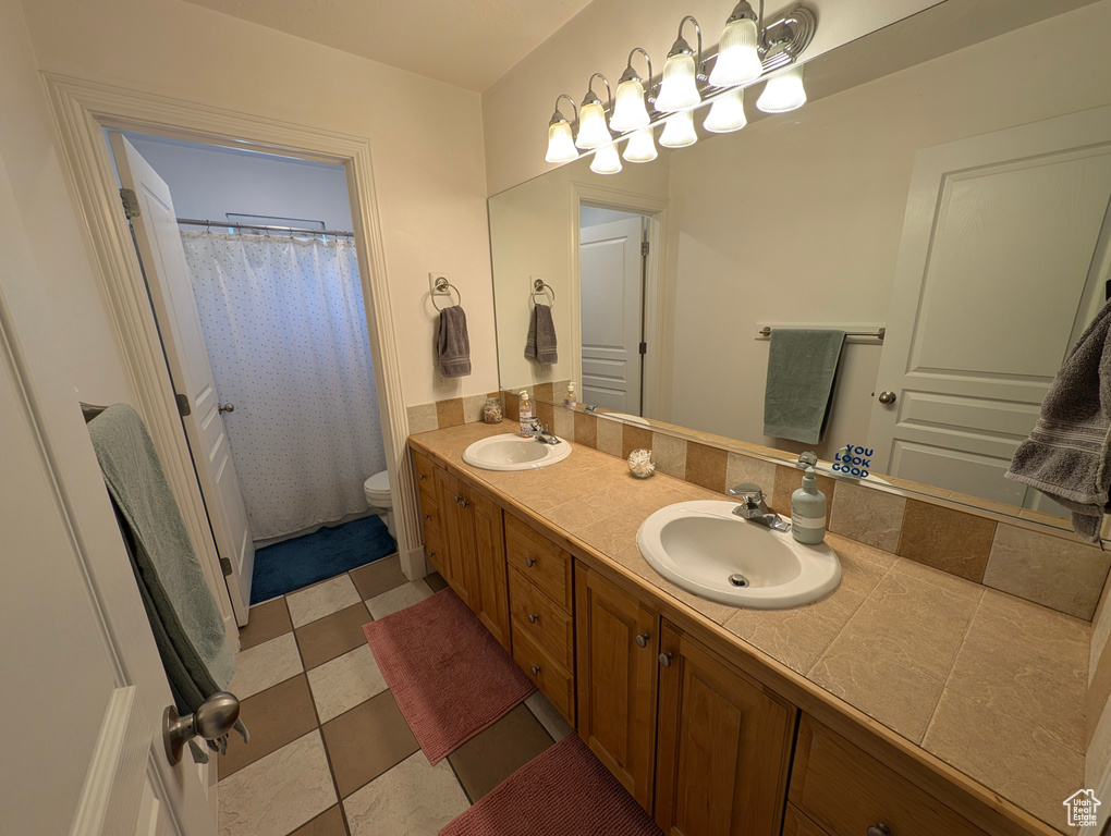 Bathroom with tile patterned flooring, toilet, and dual bowl vanity