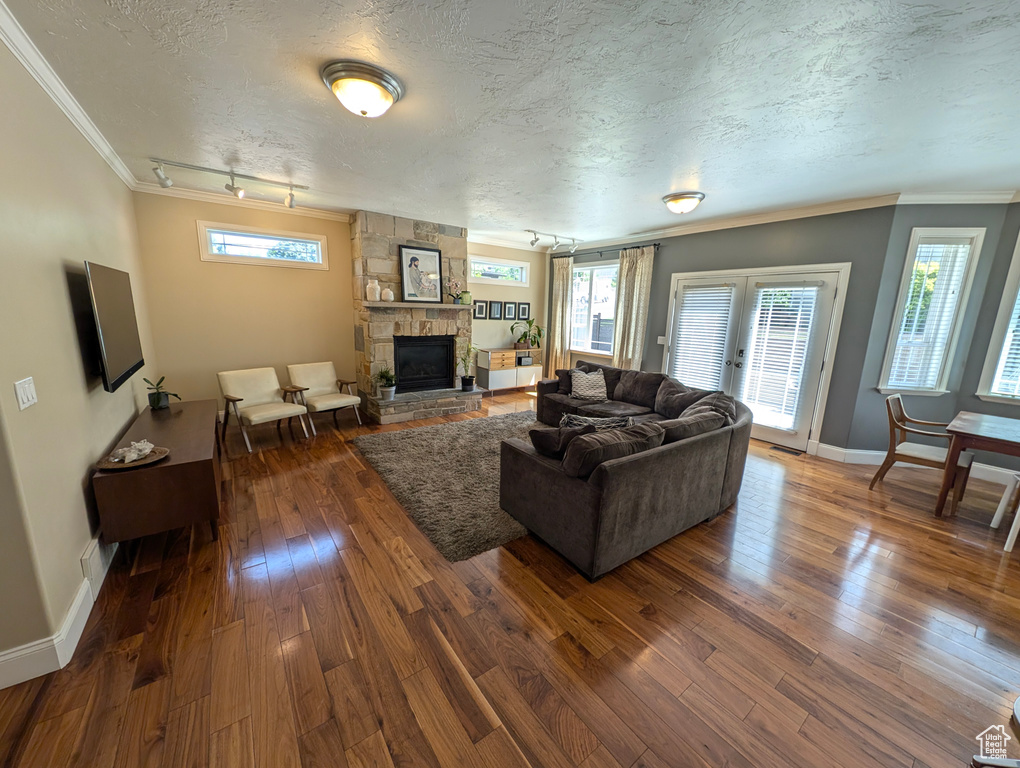 Living room featuring a stone fireplace, rail lighting, a textured ceiling, wood-type flooring, and ornamental molding