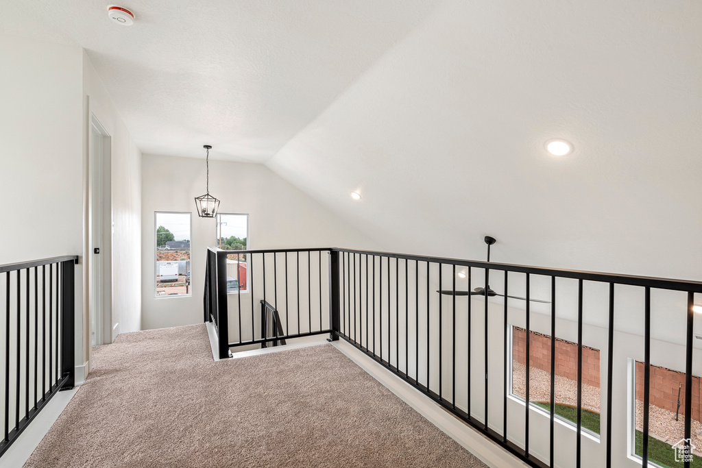 Corridor featuring an inviting chandelier, lofted ceiling, and light colored carpet