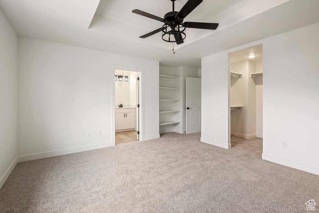 Unfurnished bedroom featuring ensuite bathroom, a closet, light colored carpet, a walk in closet, and ceiling fan