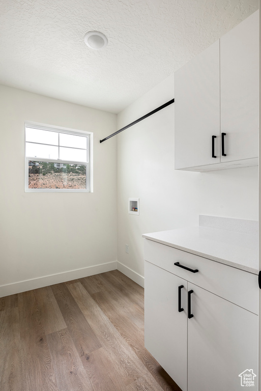 Laundry area featuring light wood-type flooring, cabinets, hookup for a washing machine, and a textured ceiling