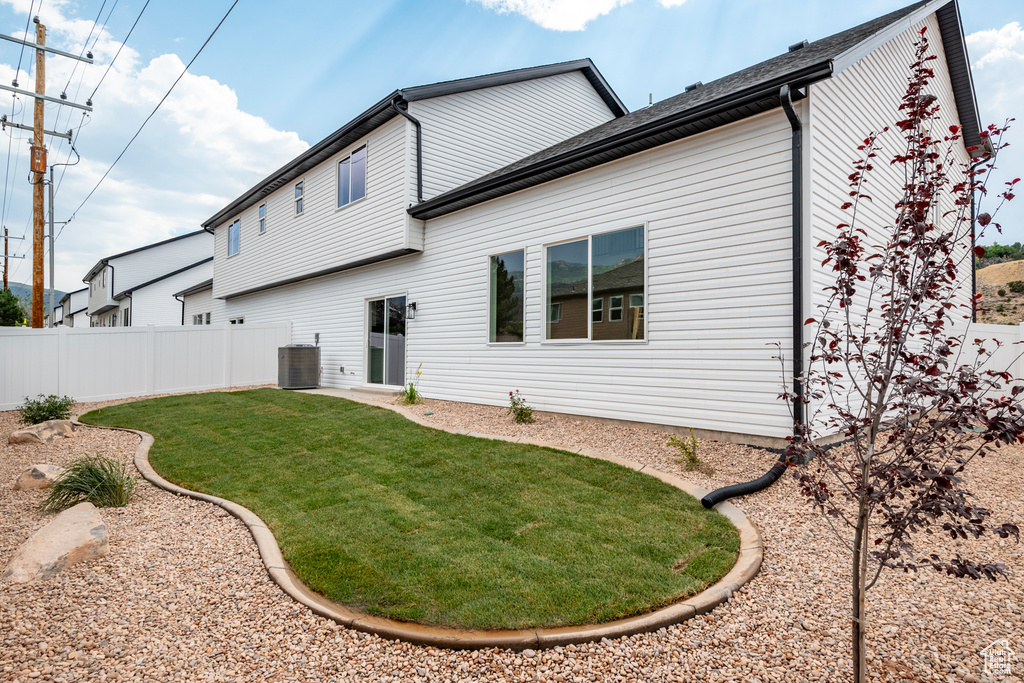 Rear view of property with central air condition unit and a lawn