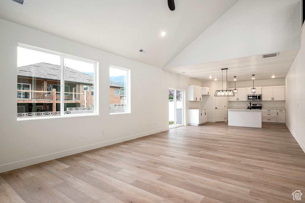 Unfurnished living room featuring high vaulted ceiling and light wood-type flooring