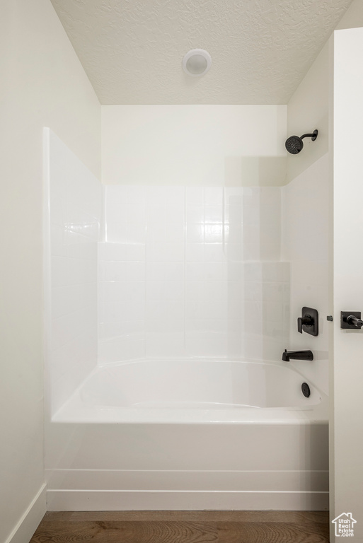 Bathroom with wood-type flooring, bathing tub / shower combination, and a textured ceiling