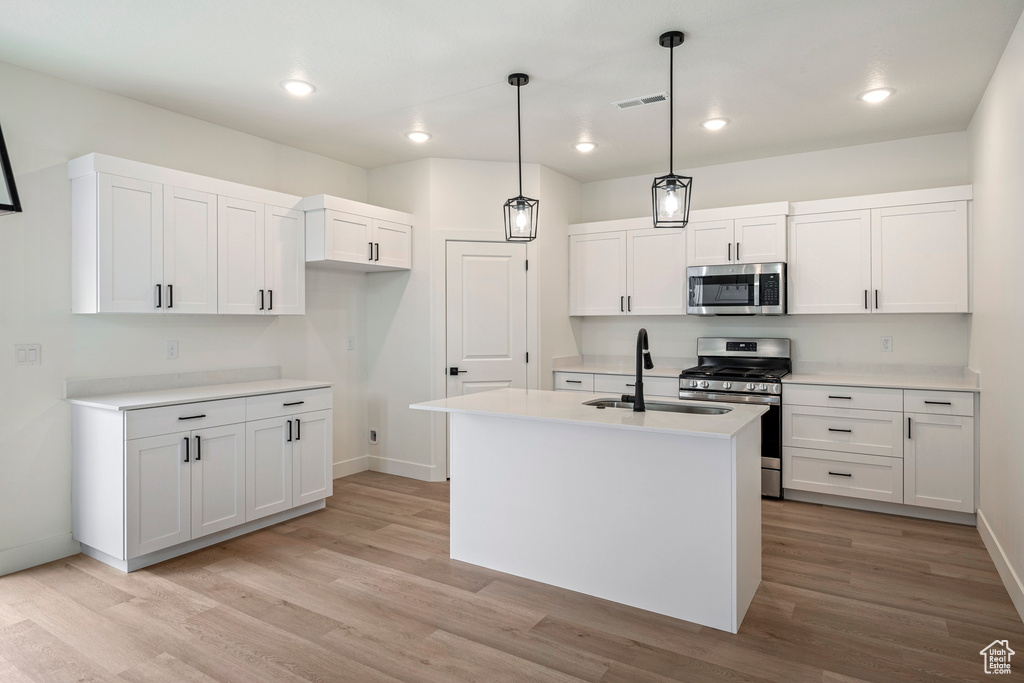 Kitchen with white cabinetry, light wood-type flooring, a kitchen island with sink, stainless steel appliances, and sink