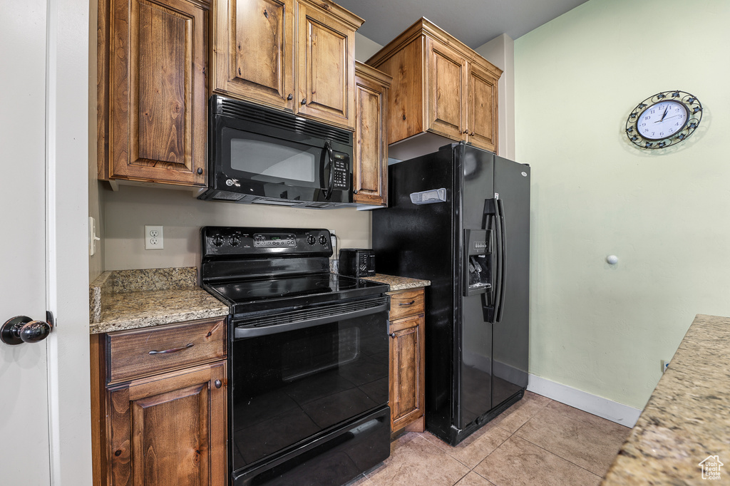 Kitchen featuring light tile patterned flooring, black appliances, and light stone counters