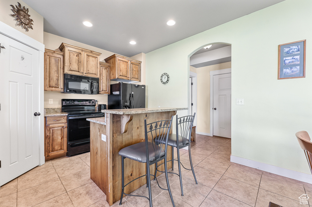 Kitchen with light tile patterned flooring, a center island, black appliances, and a breakfast bar